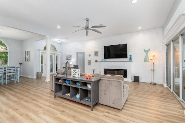 living room featuring decorative columns, recessed lighting, light wood-style flooring, a ceiling fan, and a glass covered fireplace