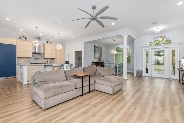 living room featuring recessed lighting, ceiling fan with notable chandelier, visible vents, light wood-style floors, and ornate columns