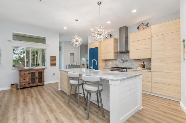 kitchen with pendant lighting, light brown cabinets, a kitchen island with sink, modern cabinets, and wall chimney exhaust hood