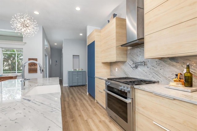 kitchen with stainless steel stove, decorative backsplash, light brown cabinetry, a sink, and wall chimney range hood