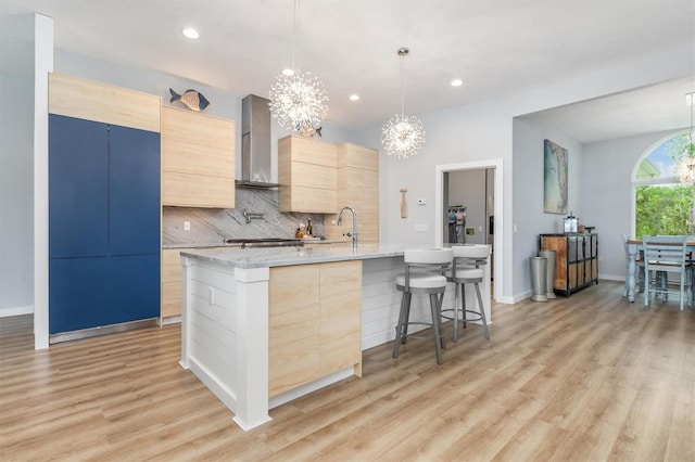 kitchen with modern cabinets, light stone counters, hanging light fixtures, light brown cabinetry, and wall chimney range hood