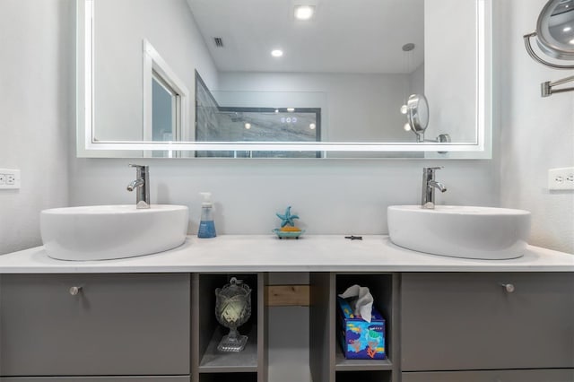 bathroom with double vanity, visible vents, a tile shower, and a sink