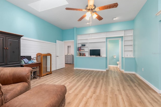 living room featuring ceiling fan, light wood finished floors, a skylight, and baseboards