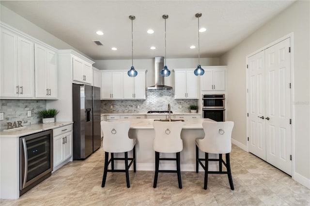 kitchen featuring decorative light fixtures, white cabinets, beverage cooler, stainless steel appliances, and wall chimney range hood