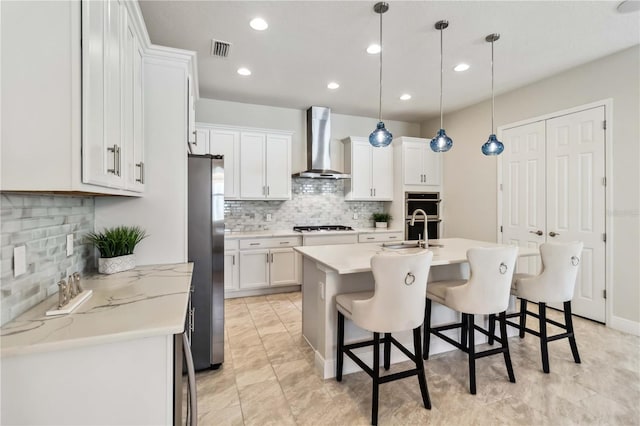 kitchen featuring wall chimney exhaust hood, gas stovetop, stainless steel refrigerator, pendant lighting, and white cabinets