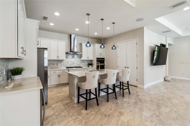 kitchen featuring a breakfast bar, wall chimney range hood, white cabinets, and stainless steel refrigerator