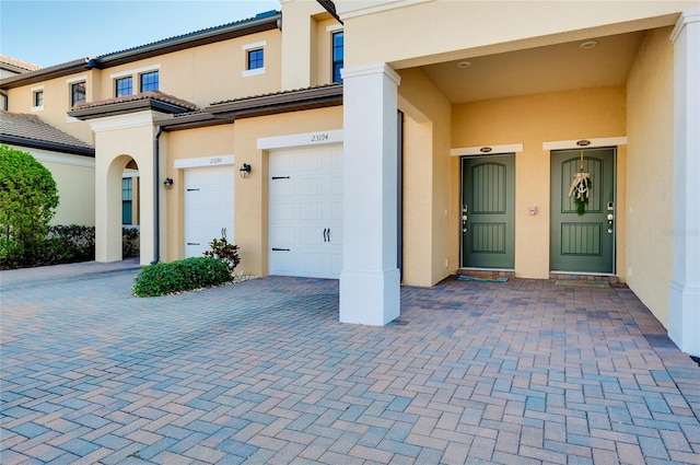 property entrance featuring decorative driveway, a tile roof, an attached garage, and stucco siding