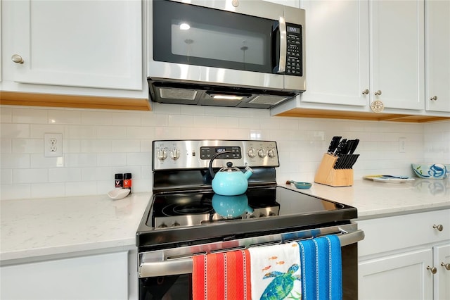 kitchen with stainless steel appliances, white cabinets, backsplash, and light stone counters