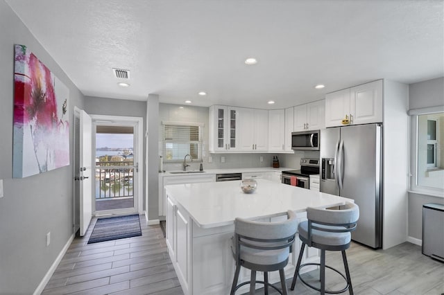 kitchen with a breakfast bar, appliances with stainless steel finishes, a center island, white cabinets, and light wood-type flooring