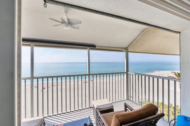 balcony with a beach view, ceiling fan, and a water view