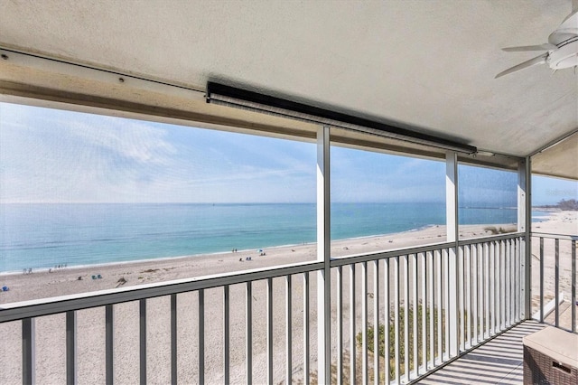 balcony with a view of the beach, ceiling fan, and a water view