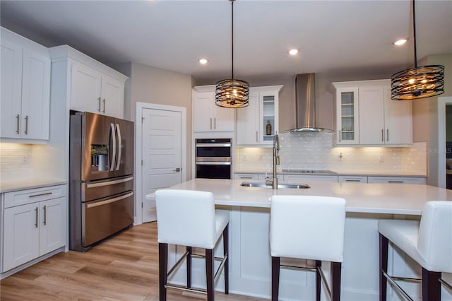 kitchen with decorative light fixtures, a breakfast bar area, stainless steel appliances, and wall chimney exhaust hood