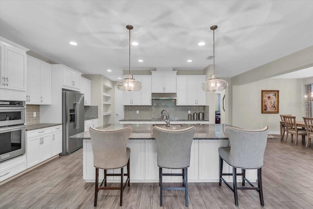 kitchen with stainless steel appliances, white cabinetry, hanging light fixtures, and a center island with sink