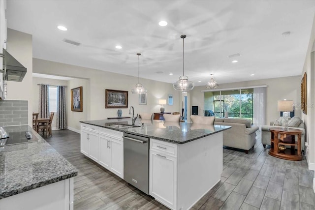 kitchen featuring sink, white cabinetry, hanging light fixtures, a center island with sink, and dark stone counters