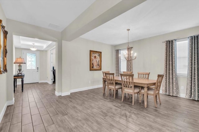 dining area featuring a raised ceiling, an inviting chandelier, and light wood-type flooring