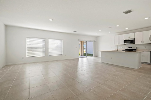 kitchen with light tile patterned floors, appliances with stainless steel finishes, a kitchen island with sink, and white cabinets