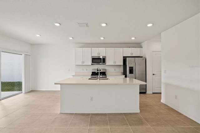 kitchen with sink, light tile patterned floors, stainless steel appliances, a kitchen island with sink, and white cabinets