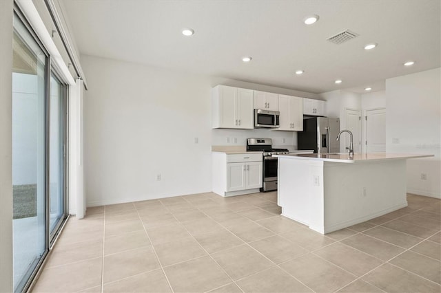 kitchen with light tile patterned flooring, sink, white cabinets, a kitchen island with sink, and stainless steel appliances