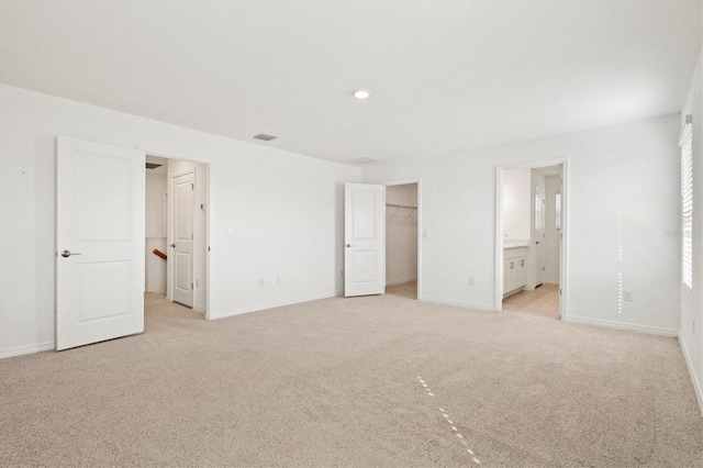 unfurnished bedroom with ensuite bath, a walk in closet, light colored carpet, and a closet