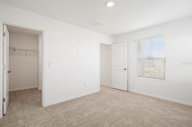 unfurnished bedroom featuring a spacious closet, light colored carpet, and a closet