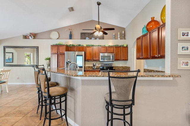 kitchen featuring appliances with stainless steel finishes, kitchen peninsula, a breakfast bar area, ceiling fan, and light stone counters