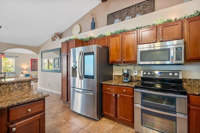 kitchen with lofted ceiling, stainless steel appliances, light tile patterned floors, and dark stone countertops