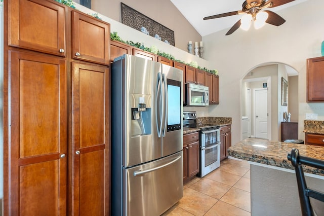 kitchen with lofted ceiling, light tile patterned floors, appliances with stainless steel finishes, ceiling fan, and dark stone counters