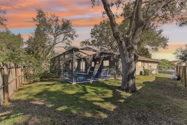 back house at dusk with a fenced in pool, a yard, and glass enclosure