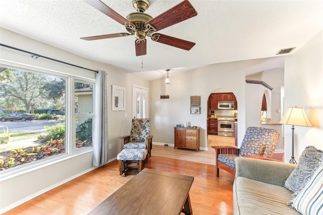 living room featuring ceiling fan, a textured ceiling, and light hardwood / wood-style floors