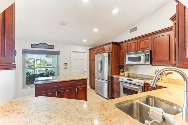 kitchen featuring lofted ceiling, sink, light stone counters, and appliances with stainless steel finishes