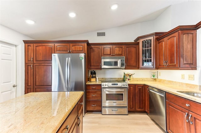 kitchen with lofted ceiling, sink, stainless steel appliances, light stone countertops, and light hardwood / wood-style floors