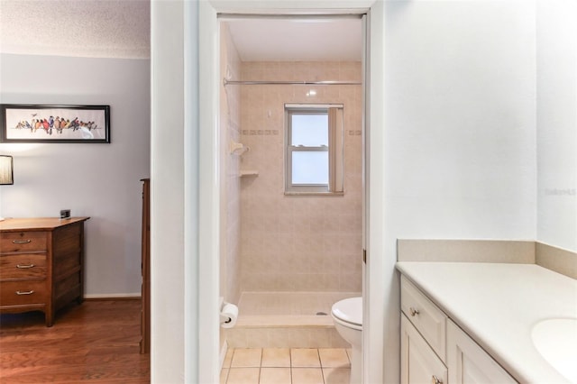 bathroom featuring a tile shower, tile patterned flooring, vanity, toilet, and a textured ceiling