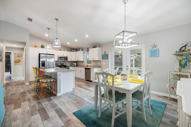 dining space with french doors, lofted ceiling, and light hardwood / wood-style floors