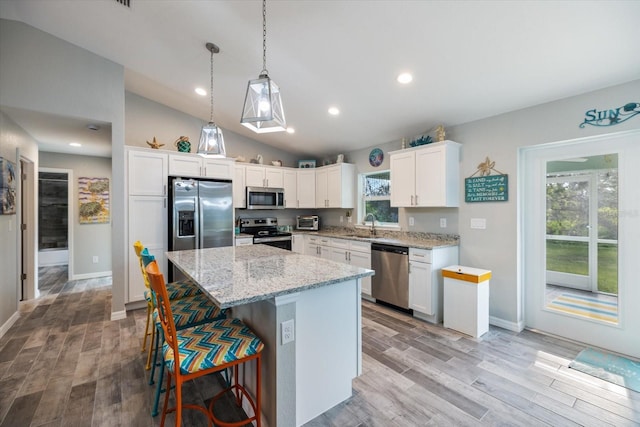 kitchen with pendant lighting, appliances with stainless steel finishes, a center island, light hardwood / wood-style floors, and white cabinets