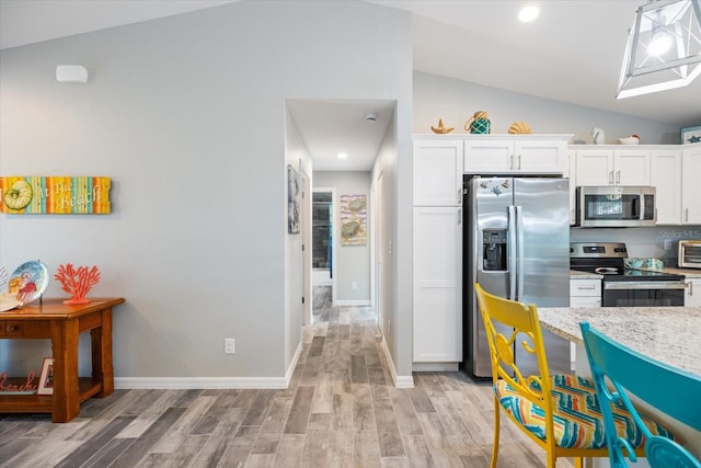 kitchen with light wood-type flooring, vaulted ceiling, white cabinets, and appliances with stainless steel finishes