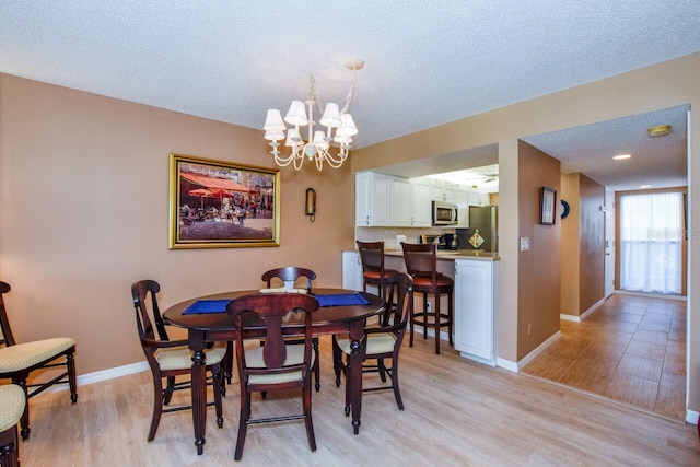 dining area with an inviting chandelier, a textured ceiling, and light wood-type flooring