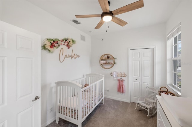 bedroom with ceiling fan, a nursery area, dark carpet, and a closet