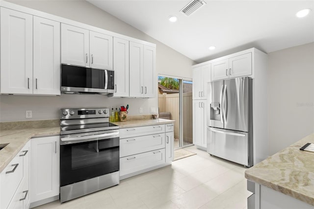 kitchen featuring vaulted ceiling, light stone countertops, appliances with stainless steel finishes, and white cabinets