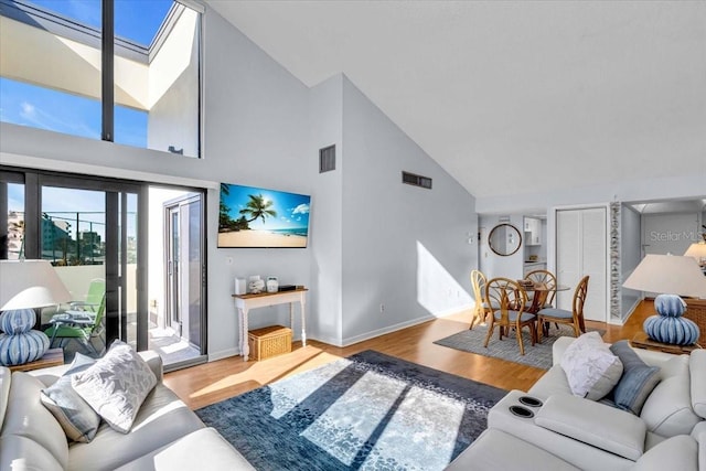 living room with hardwood / wood-style flooring, high vaulted ceiling, and a skylight