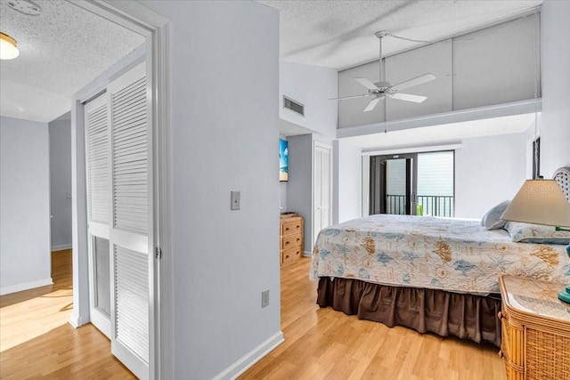 bedroom with two closets, high vaulted ceiling, access to exterior, light hardwood / wood-style floors, and a textured ceiling