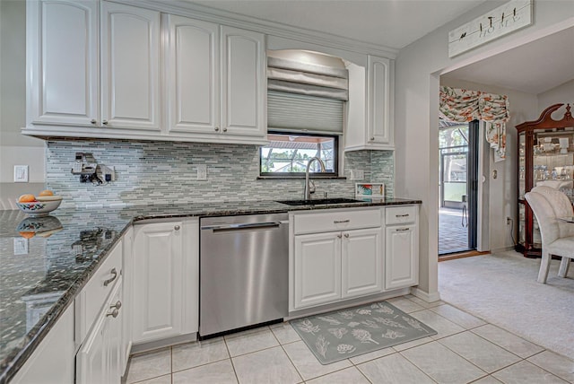 kitchen with sink, white cabinetry, dark stone countertops, stainless steel dishwasher, and light colored carpet