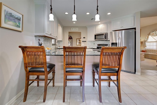 kitchen with appliances with stainless steel finishes, white cabinetry, sink, dark stone countertops, and hanging light fixtures