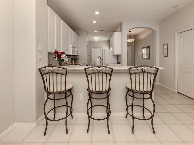 kitchen with white cabinetry, white appliances, kitchen peninsula, and a breakfast bar area