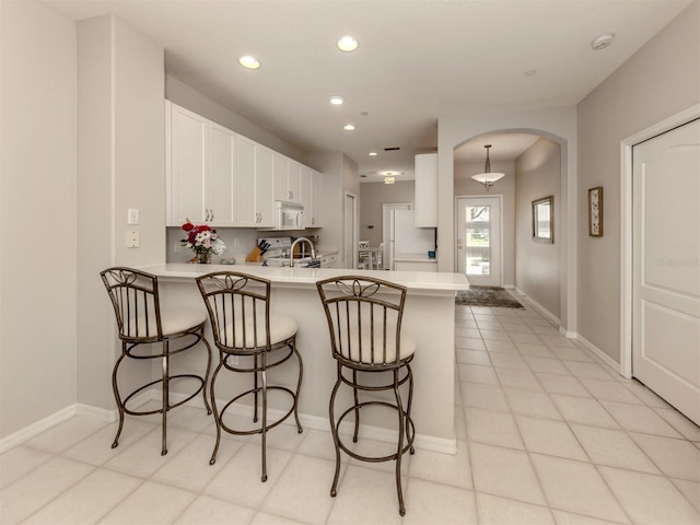 kitchen featuring sink, white appliances, a breakfast bar area, white cabinets, and kitchen peninsula