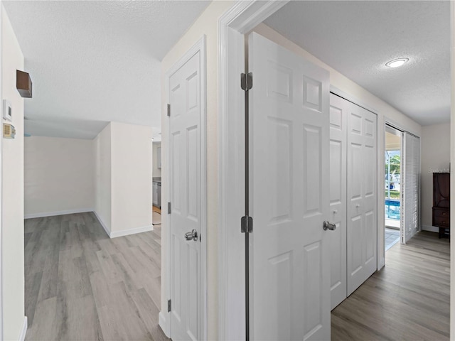 corridor with a textured ceiling and light hardwood / wood-style floors