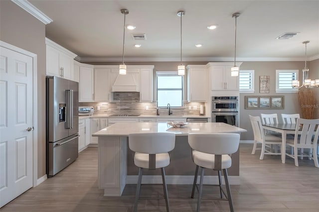 kitchen with decorative light fixtures, a kitchen island, white cabinets, and appliances with stainless steel finishes