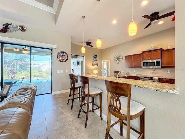 kitchen with pendant lighting, appliances with stainless steel finishes, a breakfast bar area, and light stone counters