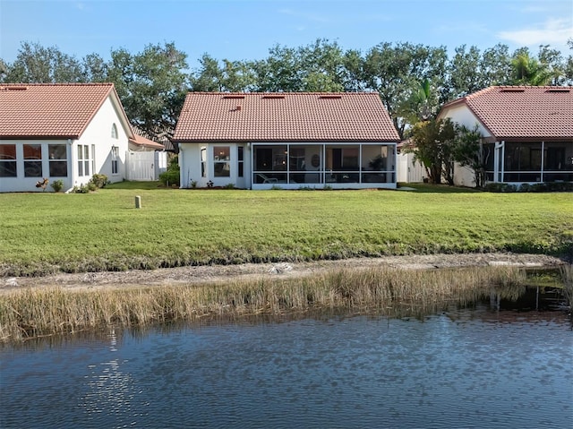 rear view of property featuring a water view, a sunroom, and a yard