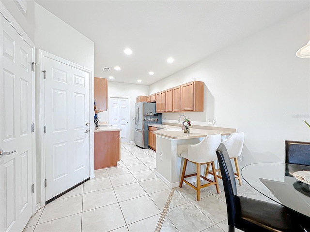 kitchen featuring stainless steel refrigerator, light tile patterned flooring, kitchen peninsula, and sink