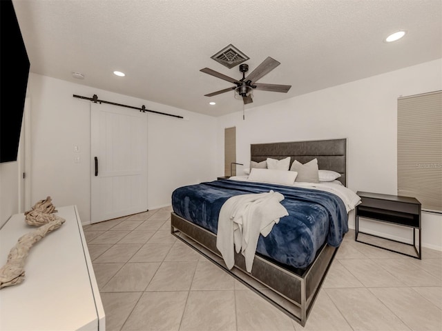 tiled bedroom featuring ceiling fan, a barn door, and a textured ceiling